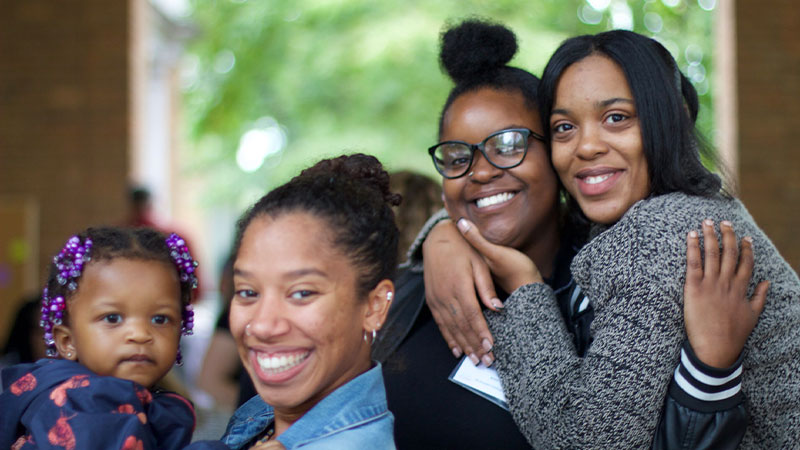 Three women and a baby smiling and hugging each other, radiating joy and love.