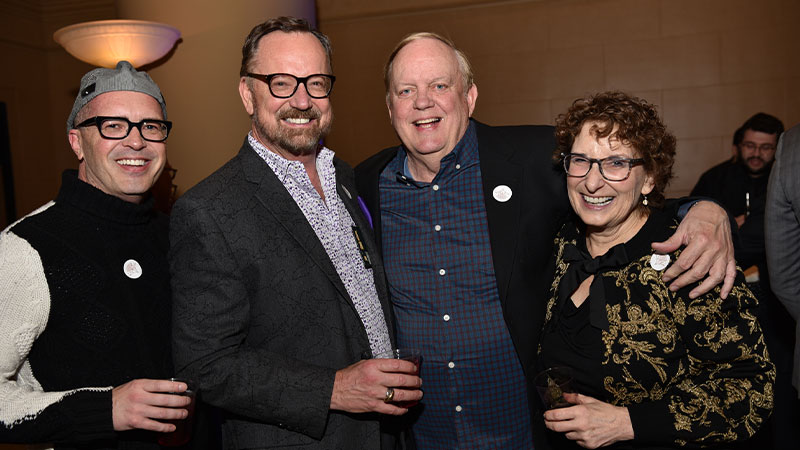 Three men and a woman smiling for a photo at an event, capturing a joyful moment of togetherness.